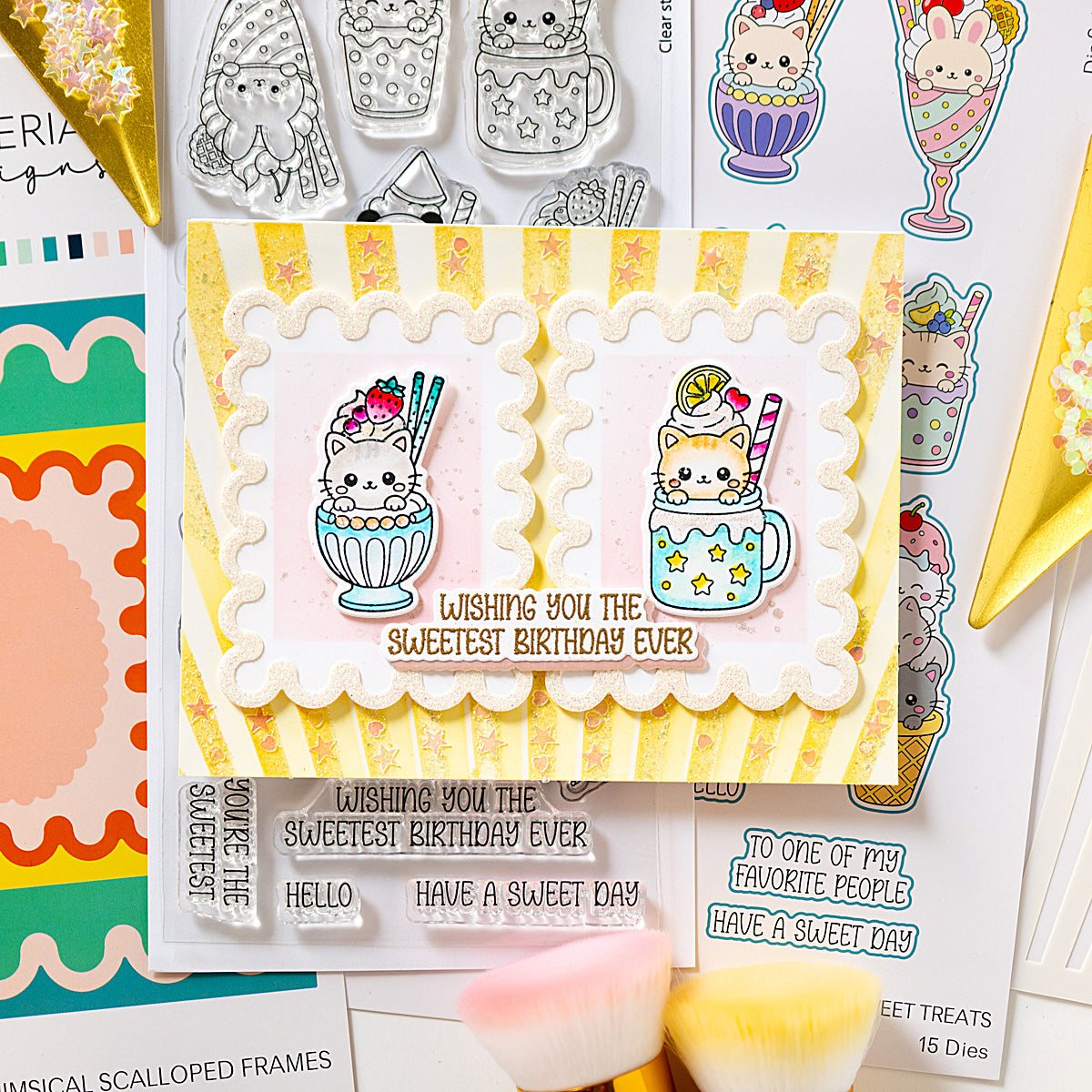 A handmade greeting card featuring two cute cartoon cats in milk tea sunda cups, with the text 'Wishing you the SWEETEST birthday ever' in brown script. The card is styled on a flat-lay of craft supplies, including other cards, stickers, and small brushes. Sweet treats alex syberia designs stamp