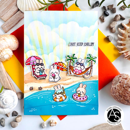 A square handmade greeting card featuring a beach scene with cartoon rabbits relaxing by the shore, surrounded by seashells and colorful paper accents. The card has the text 'JUST KEEP CHILLIN' and a circular 'AS Creative Team' logo in the bottom right corner. Alex Syberia Designs